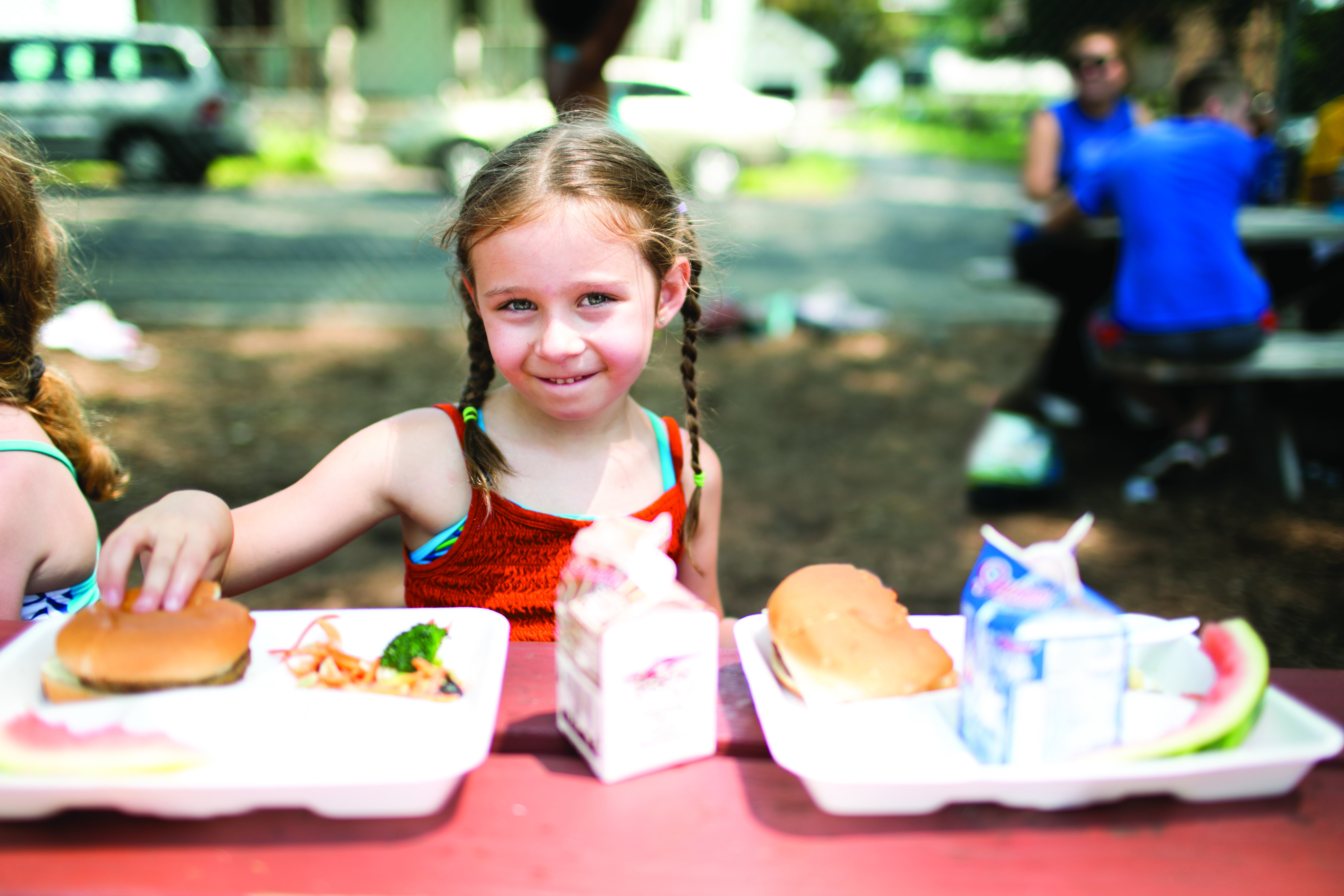 Young girl at a picnic table with a lunch tray and milk carton.