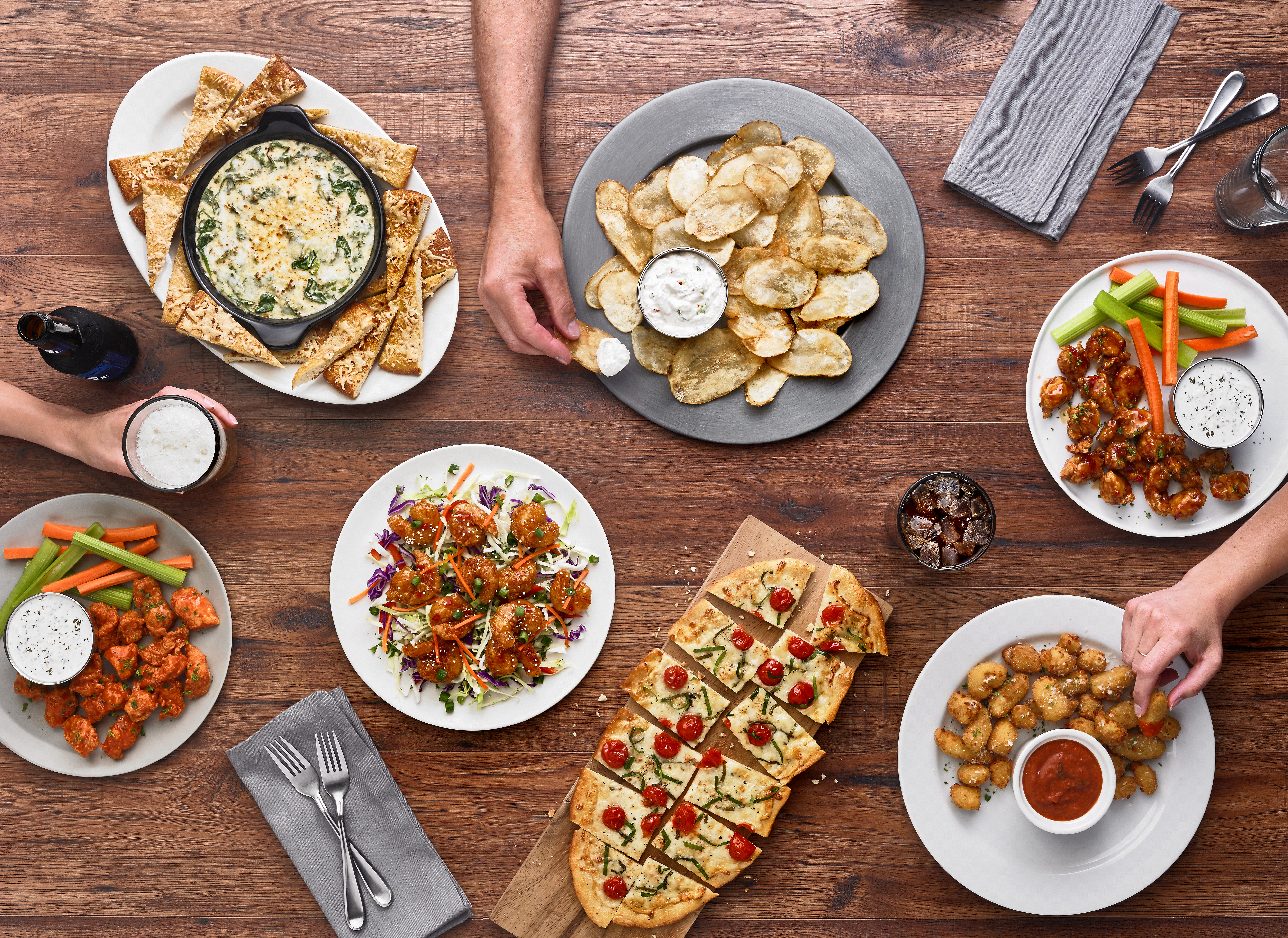 various dishes and drinks on top of a table with hands reaching out