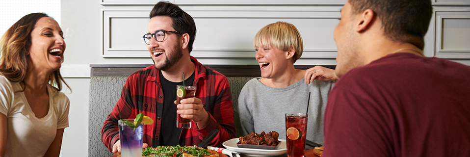 Four friends laugh while enjoying food and drinks at Boston's.