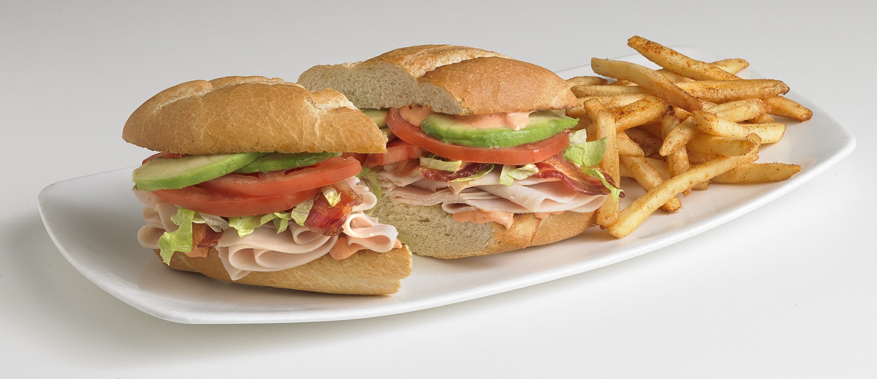 The Turkey-Bacon-Avocado Sandwich, cut in two, served on a plate with seasoned fries.