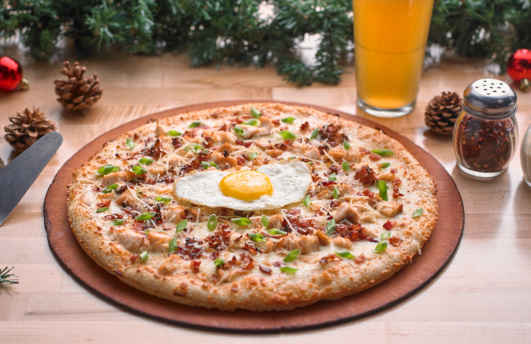 Pizza with chicken, bacon, and a sunny side egg on a wooden table