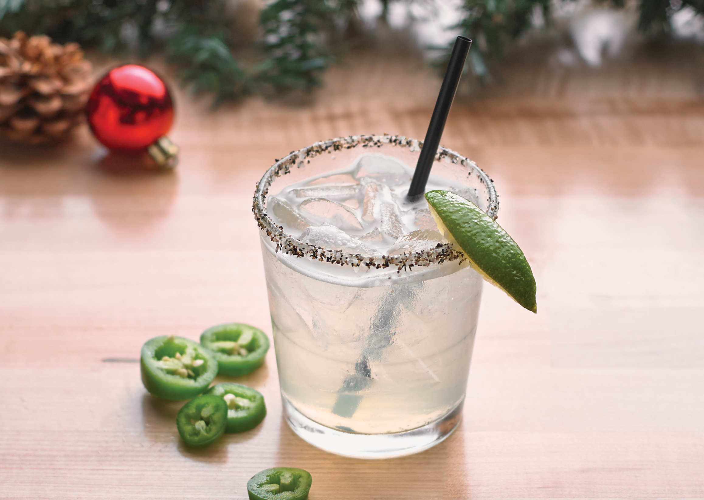A tequila cocktail with a lime slice on a wood table, with Christmas garland around it