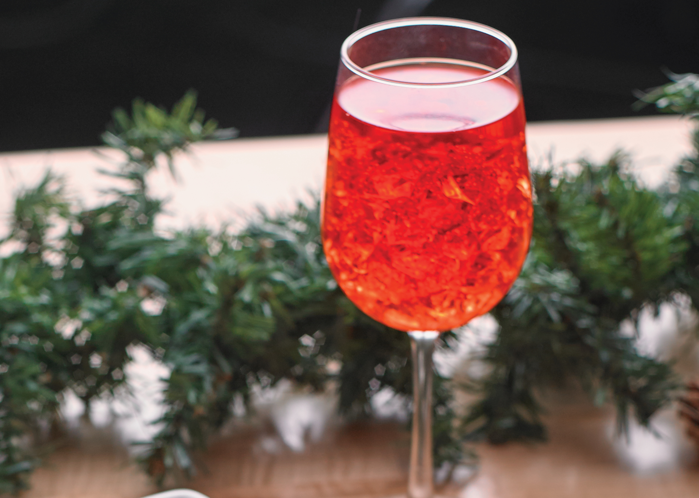 Red Aperol Spritz on a wood table with christmas garland in the background