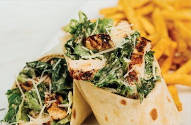 image of grilled chicken caesar salad wrapped in a tortilla. Served with a side of fries.