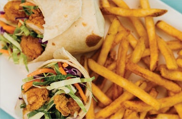 Image of fried chicken wrap with colelsaw. Served with a side of fries.